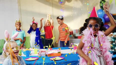 Animation-of-gold-confetti-falling-over-happy-diverse-children-dancing-with-streamers-at-party