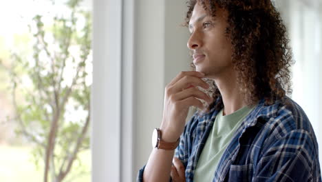 Portrait-of-thoughtful-biracial-man-with-long-curly-hair-by-window-at-home,-copy-space,-slow-motion