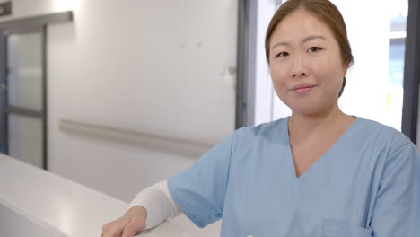 Retrato-De-Una-Feliz-Doctora-Asiática-Usando-Una-Tableta-En-La-Recepción-Del-Hospital,-Cámara-Lenta