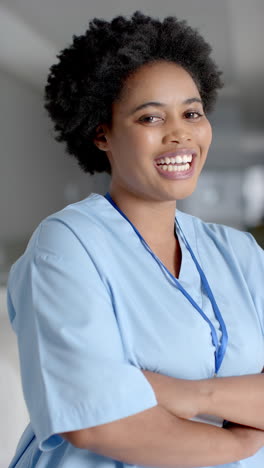Vertical-video-of-portrait-of-happy-african-american-female-doctor-in-hospital-corridor,-slow-motion
