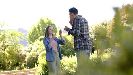 Happy-diverse-couple-blowing-bubbles-in-sunny-garden,-in-slow-motion