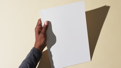 Video-of-hand-of-african-american-man-holding-book-with-blank-pages,-copy-space-on-yellow-background