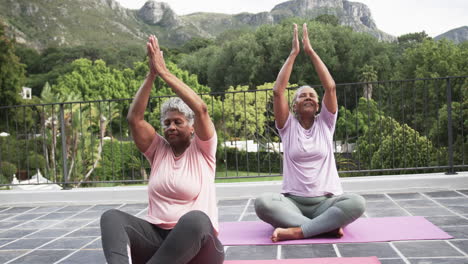 Senior-african-american-female-friends-practicing-yoga-meditation-sitting-on-balcony,-slow-motion