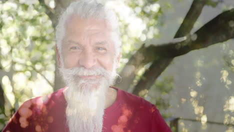 Animation-of-spots-of-light-and-trees-over-smiling-senior-biracial-man-in-garden