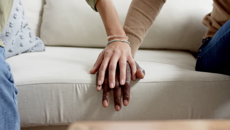 Biracial-couple-sitting-on-couch-and-holding-hands-at-home,-slow-motion