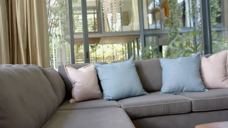 Brown-couch-with-pillows,-gold-curtains-and-huge-windows-in-sunny-living-room,-slow-motion