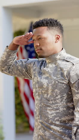 Vertical-video-of-happy-african-american-male-soldier-saluting-at-home,-slow-motion