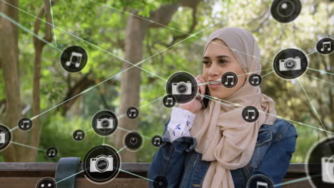 Animation-of-network-of-connected-icons-in-circles-over-happy-biracial-woman-using-smartphone