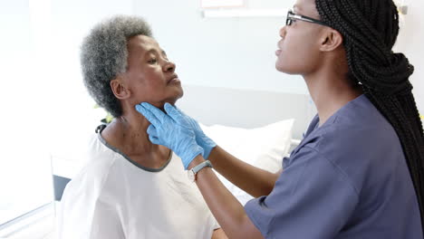 African-american-female-doctor-testing-neck-of-senior-female-patient-in-hospital-room,-slow-motion