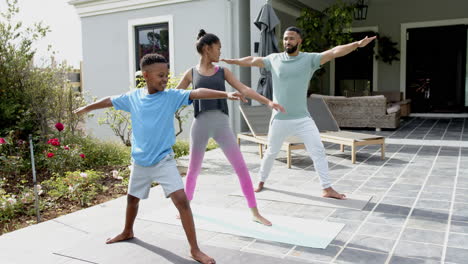 Happy-african-american-father,-son-and-daughter-practicing-yoga-standing-in-garden,-slow-motion