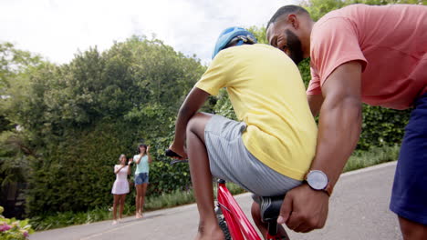 African-american-father-teaching-son-to-ride-bicycle,-mother-and-sister-clapping,-slow-motion