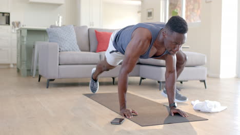 Focused-african-american-man-doing-mountain-climbers-with-smartphone-in-living-room,-slow-motion