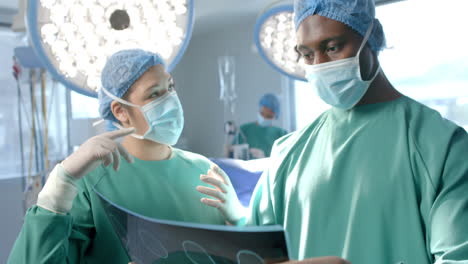 Diverse-female-and-male-surgeon-in-masks-discussing-x-ray-in-theatre,-slow-motion