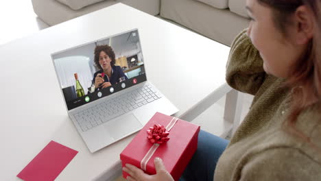 Caucasian-woman-holding-red-gift-using-laptop-with-biracial-man-on-screen