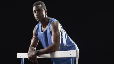 African-American-athlete-leaning-on-hurdles-at-the-gym-on-a-black-background