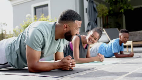 Happy-african-american-father,-son-and-daughter-exercising-in-garden-doing-plank,-slow-motion