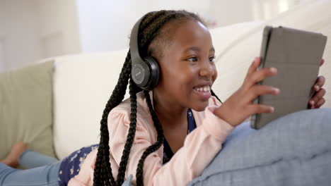 Happy-african-american-girl-with-headphones-using-tablet-at-home,-slow-motion