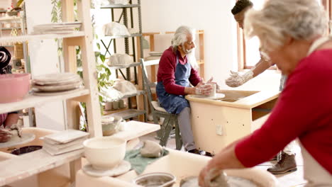 Focused-biracial-male-and-female-potters-using-potter's-wheel-in-pottery-studio,-slow-motion