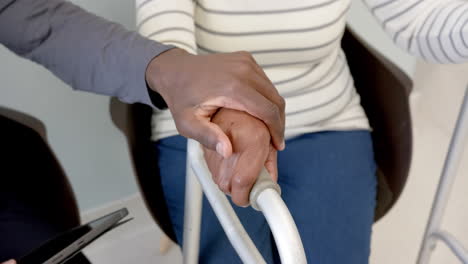 African-american-male-doctor-using-tablet-and-holding-hand-of-senior-woman-in-hospital,-slow-motion
