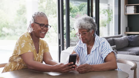 Happy-senior-african-american-female-friends-using-smartphone-and-talking-at-home,-slow-motion