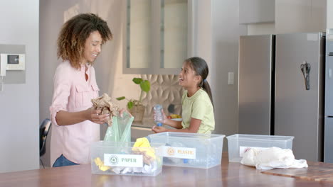 Happy-biracial-mother-and-daughter-sorting-rubbish-for-recycling-in-kitchen,-copy-space,-slow-motion