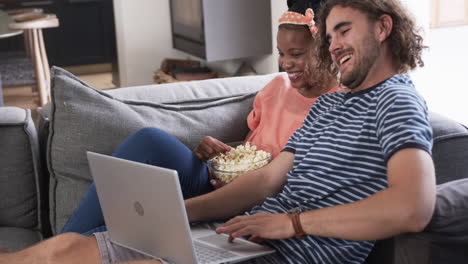 Diverse-couple,-a-young-African-American-woman-and-Caucasian-man,-enjoy-a-movie-at-home