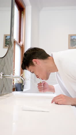 Video-Vertical-De-Un-Hombre-Birracial-Cepillándose-Los-Dientes-En-El-Baño-Por-La-Mañana,-Cámara-Lenta