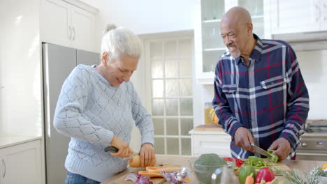 Happy-senior-diverse-couple-talking-and-cutting-vegetables-in-kitchen,-slow-motion