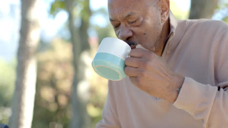 Glücklicher-älterer-Mann-Mit-Gemischter-Abstammung,-Der-Sein-Smartphone-Benutzt-Und-Zu-Hause-Auf-Dem-Balkon-Kaffee-Trinkt,-Zeitlupe