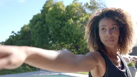 Happy-biracial-woman-practicing-yoga-stretching-arms-in-sunny-garden,-slow-motion