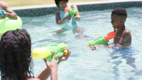 Happy-african-american-parents,-son-and-daughter-playing-with-water-pistols-in-pool,-slow-motion