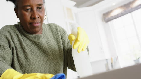 Glückliche-Afroamerikanische-Seniorin-Putzt-Theke-Und-Lächelt-In-Sonniger-Küche,-Zeitlupe