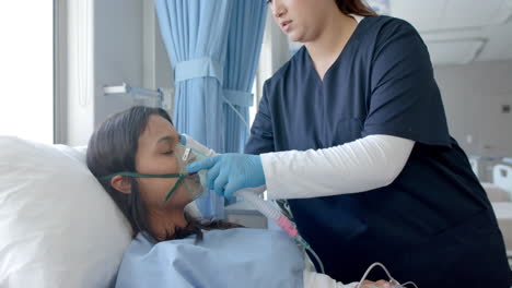 Diverse-female-doctor-putting-oxygen-mask-on-female-patient-in-hospital-bed,-slow-motion