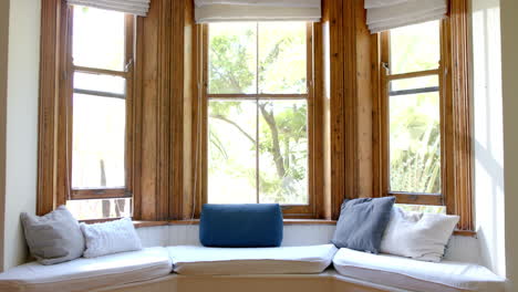 Großes-Wohnzimmer-Mit-Couch-Und-Tabletts-An-Großen-Holzfenstern