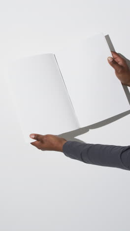 Vertical-video-of-hands-of-african-american-man-with-book-with-white-blank-pages-on-white-background