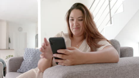 Happy-plus-size-biracial-woman-having-smartphone-video-call-sitting-on-sofa-at-home,-slow-motion