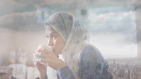 Animation-Einer-Stadtlandschaft-über-Einer-Gemischtrassigen-Frau-Im-Hijab,-Die-Tee-Trinkt