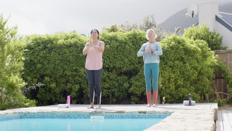 Zwei-Glückliche,-Vielfältige-Seniorinnen-Praktizieren-Yoga-Am-Pool-Im-Sonnigen-Garten,-Zeitlupe,-Kopierraum