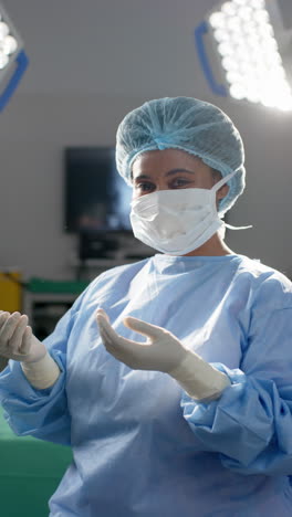 Vertical-video-of-portrait-of-african-american-female-surgeon-in-operating-theatre,-slow-motion