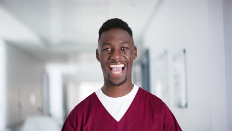 Portrait-of-happy-african-american-male-doctor-wearing-scrubs-in-hospital,-slow-motion