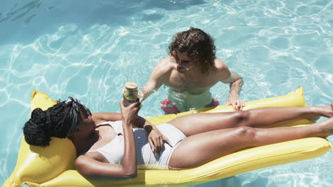 Diverse-couple,-a-young-African-American-woman-and-Caucasian-man,-enjoy-a-sunny-pool-day