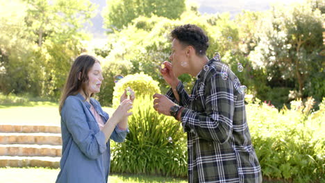 Happy-diverse-couple-blowing-bubbles-in-sunny-garden,-in-slow-motion