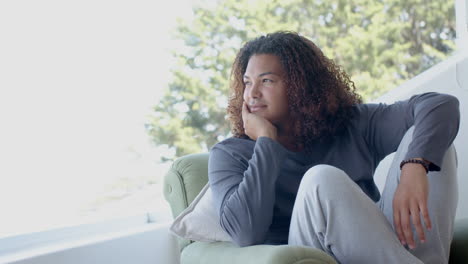 Happy-biracial-man-with-long-hair-sitting-in-sunny-room-enjoying-view,-copy-space,-slow-motion