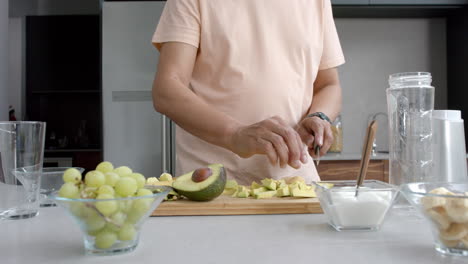 Midsection-of-senior-biracial-man-chopping-fruit-and-vegetables-for-smoothie-in-kitchen,-slow-motion
