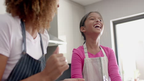 Happy-biracial-mother-and-daughter-having-fun-and-baking-in-kitchen,-slow-motion