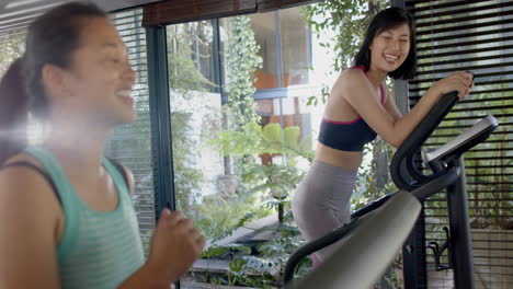 Happy-asian-female-friends-exercising-and-smiling-in-sunny-home-gym,-slow-motion