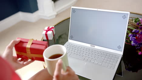 Hands-of-biracial-teenage-girl-with-gift-having-laptop-video-call,-copy-space-screen,-slow-motion