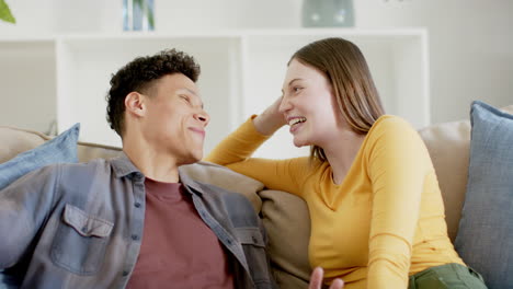 Happy-diverse-couple-sitting-on-sofa-talking-and-laughing-at-home,-in-slow-motion