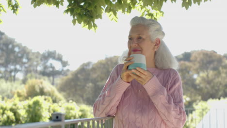 Happy-senior-biracial-woman-drinking-coffee-at-balcony-at-home,-slow-motion