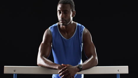 Atleta-Afroamericano-Descansando-Sobre-Los-Obstáculos-Sobre-Un-Fondo-Negro